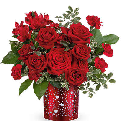 Short red rose arrangement with red accent flowers in a red heart-patterned vase