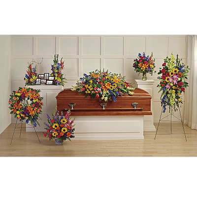 Colorful funeral floral set with casket spray, standing sprays, wreath, and vase arrangements around a wooden casket.