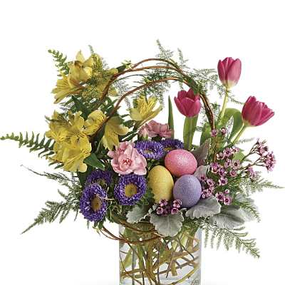 Easter floral arrangement with pink tulips, yellow blooms, purple flowers and pastel eggs in a clear glass vase