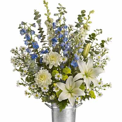 Tall arrangement of white lilies, mums, and blue delphinium in a metal bucket vase