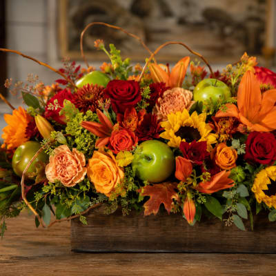 Autumn floral centerpiece with sunflowers, roses, lilies, and green apples in a wooden box