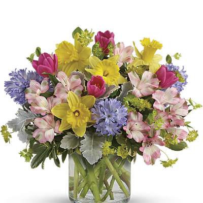 Bright spring bouquet of yellow daffodils, pink tulips, and mixed blooms in a clear glass vase
