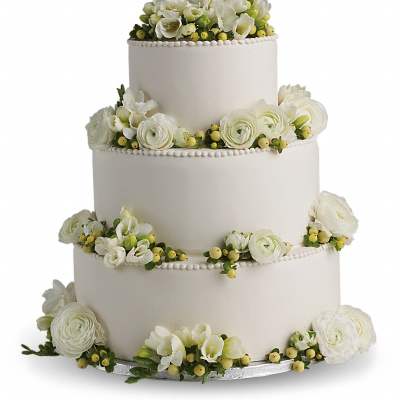 Four-tier white wedding cake decorated with white flowers and green berries around each layer