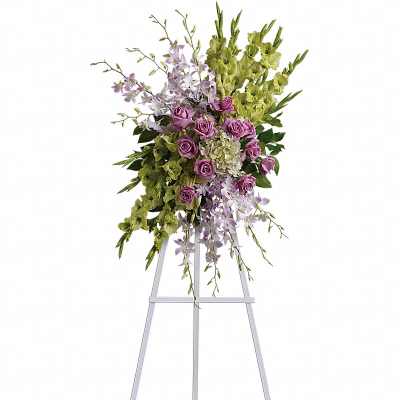 Tall sympathy spray of lavender roses, orchids, and green blooms on a white easel stand
