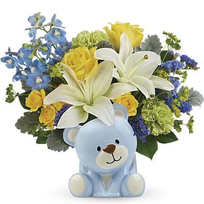 Mixed bouquet of white lilies, yellow roses, and blue flowers arranged in a light blue ceramic bear container