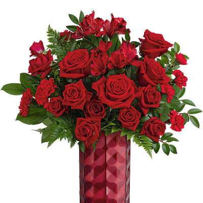 Tall arrangement of red roses, carnations, and alstroemeria in a faceted red glass vase