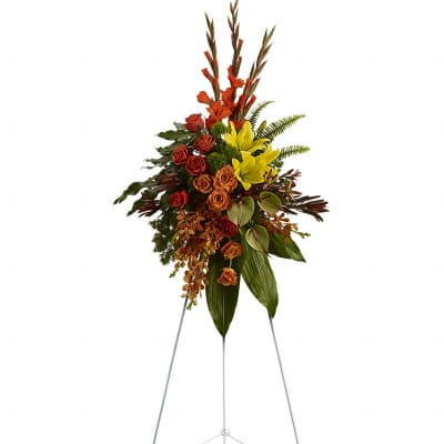 Tall standing spray of orange roses, yellow lilies, and gladiolus on a metal easel