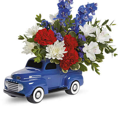 Red, white, and blue flower arrangement in a blue ceramic pickup truck container