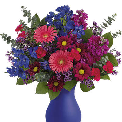 Vibrant bouquet of pink gerbera daisies, blue delphinium, and mixed blooms in a matte cobalt blue vase