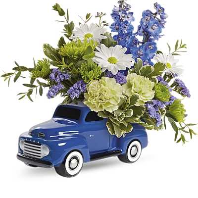 Arrangement of white daisies, green carnations, and blue flowers in a blue ceramic truck container