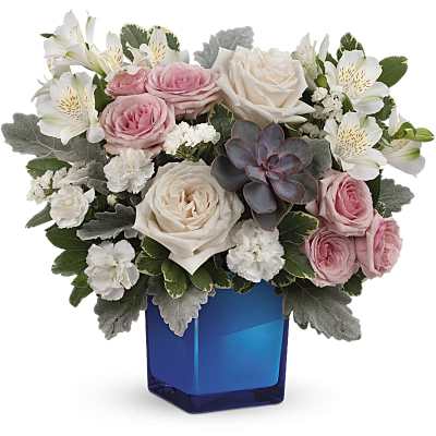 Short arrangement of pink and cream roses with white alstroemeria and a succulent in a blue cube vase