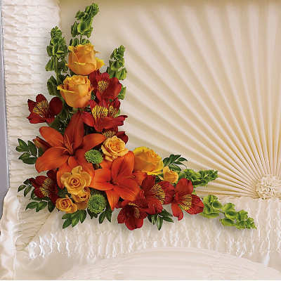 Casket corner spray with orange lilies, yellow roses, and red flowers on ivory fabric