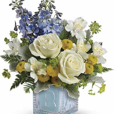 White roses, blue delphinium, and yellow button mums in a blue glass baby block vase