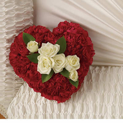 Heart-shaped red carnation floral piece with white roses resting on white satin fabric