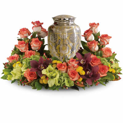 Cremation urn surrounded by a ring of peach roses, green hydrangeas, yellow mums, and burgundy orchids.
