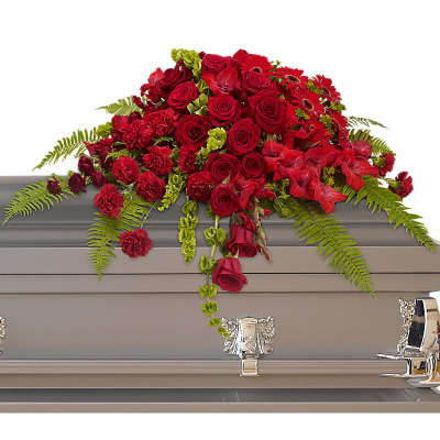 Red rose and carnation casket spray draping over a gray casket