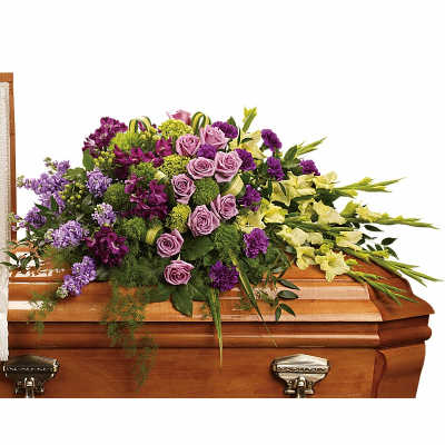 Purple and yellow floral casket spray with roses arranged on a wooden casket