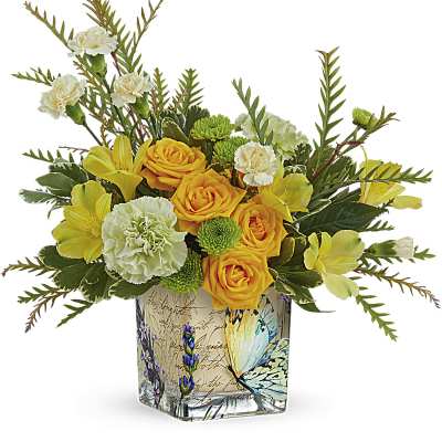 Short arrangement of yellow roses, white carnations, and green blooms in a butterfly-print square glass vase