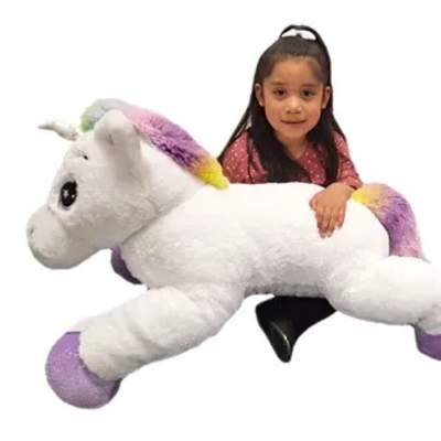 Girl hugging a large white unicorn plush toy with rainbow accents