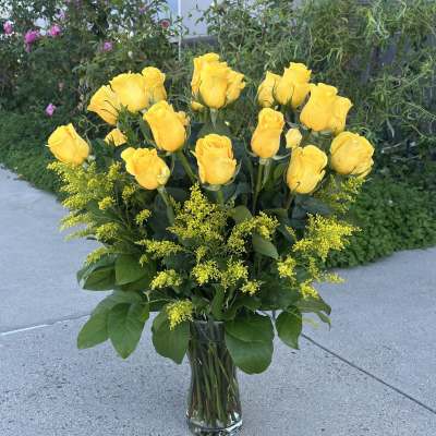 Yellow roses arranged in a clear glass vase with yellow filler flowers