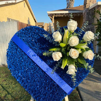 Blue heart-shaped floral tribute with white roses and lilies on an easel