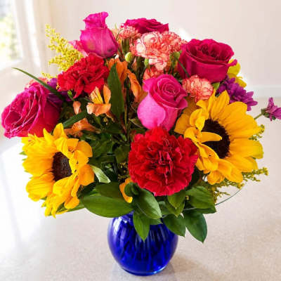 Mixed bouquet of roses, sunflowers, and carnations in a blue glass vase