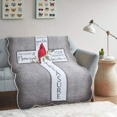 Gray quilted throw blanket with a cardinal and cross design on a sofa
