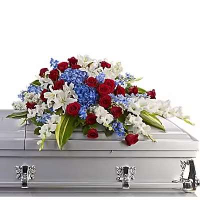 Red roses, white lilies, and blue flowers arranged on a silver casket