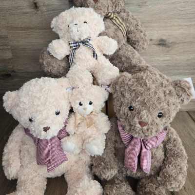Four plush teddy bears with ribbon bows arranged on a wooden floor