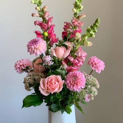 Pink and peach flowers arranged in a tall white vase