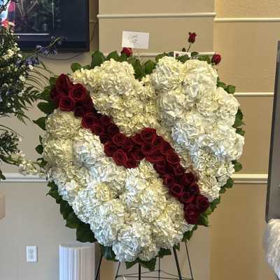 Heart-shaped floral tribute of white hydrangeas and red roses on an easel