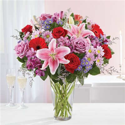 Mixed bouquet of roses, lilies, and daisies in a clear glass vase