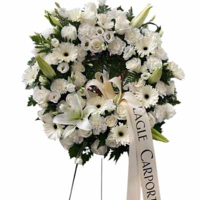 White funeral wreath with lilies, roses, and daisies on a stand
