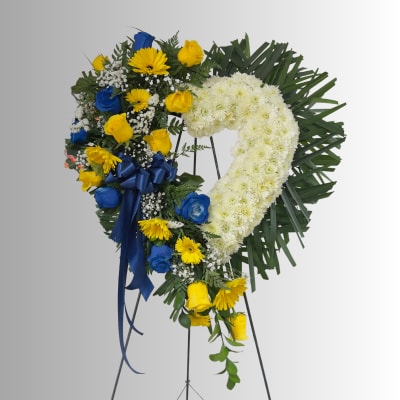 Heart-shaped floral wreath with white chrysanthemums, yellow and blue roses, and a blue ribbon
