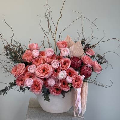 Pink floral arrangement in a white vase with tall curly branches