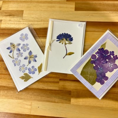 Three pressed-flower greeting cards on a wooden surface.