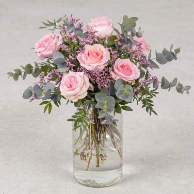 Pink roses in a clear glass vase with purple filler and eucalyptus