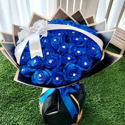 Bouquet of bright blue roses wrapped in black paper with a white ribbon