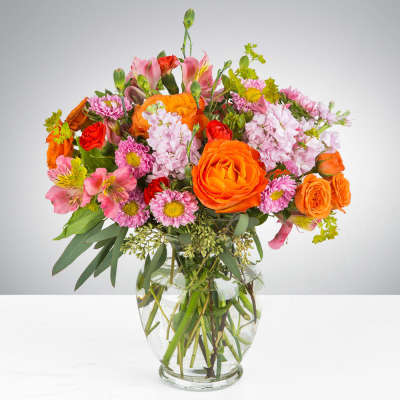 Mixed bouquet of orange, pink, and red flowers in a clear glass vase