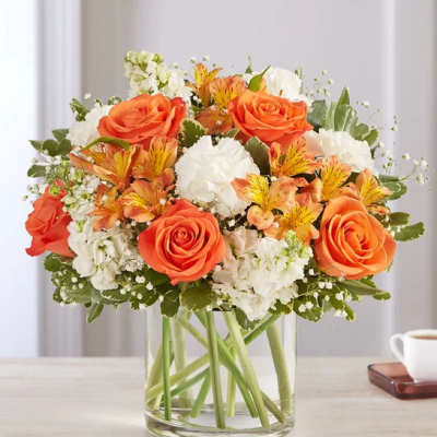 Orange roses and white flowers arranged in a clear glass vase