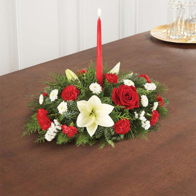 Low holiday centerpiece with red and white flowers and a red taper candle
