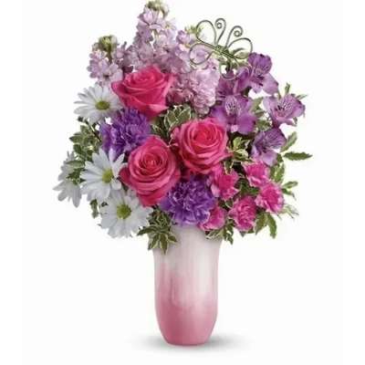 Pink roses, purple blooms, and white daisies in a pink ombré vase with a metal butterfly accent