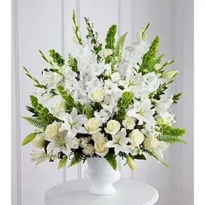 Large white arrangement of lilies and roses in a white pedestal vase