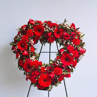 Heart-shaped red floral wreath on a black stand