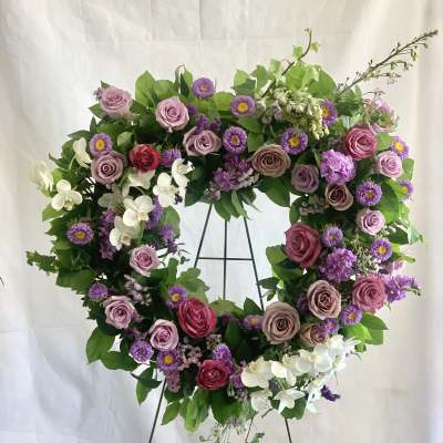 Heart-shaped floral wreath with pink and purple flowers on a metal stand