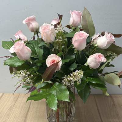 Pink roses arranged in a clear glass vase with greenery