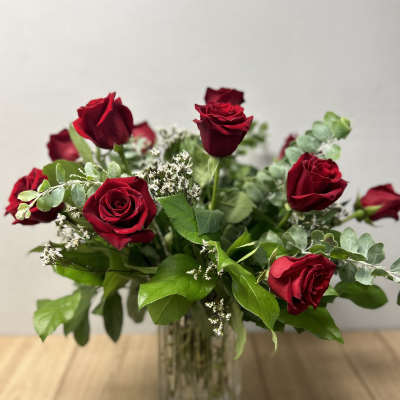 Red roses arranged in a clear glass vase with greenery