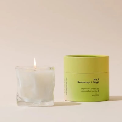 Lit white candle in a clear glass vessel beside a lime-green candle tin