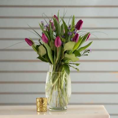 Pink tulips arranged in a clear glass vase with small purple filler flowers