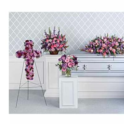 Floral funeral display with a cross, casket spray, and standing sprays in pink and purple